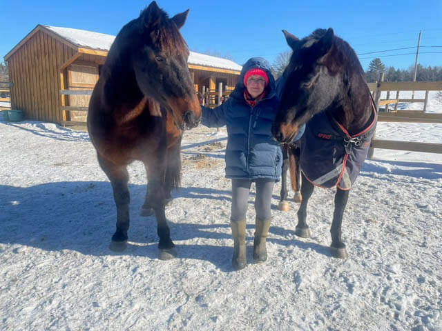 A woman getting hugs from horses in the snow